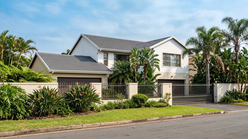 A cream plastered Durban home with a tiled roof among palms and strelitzias.